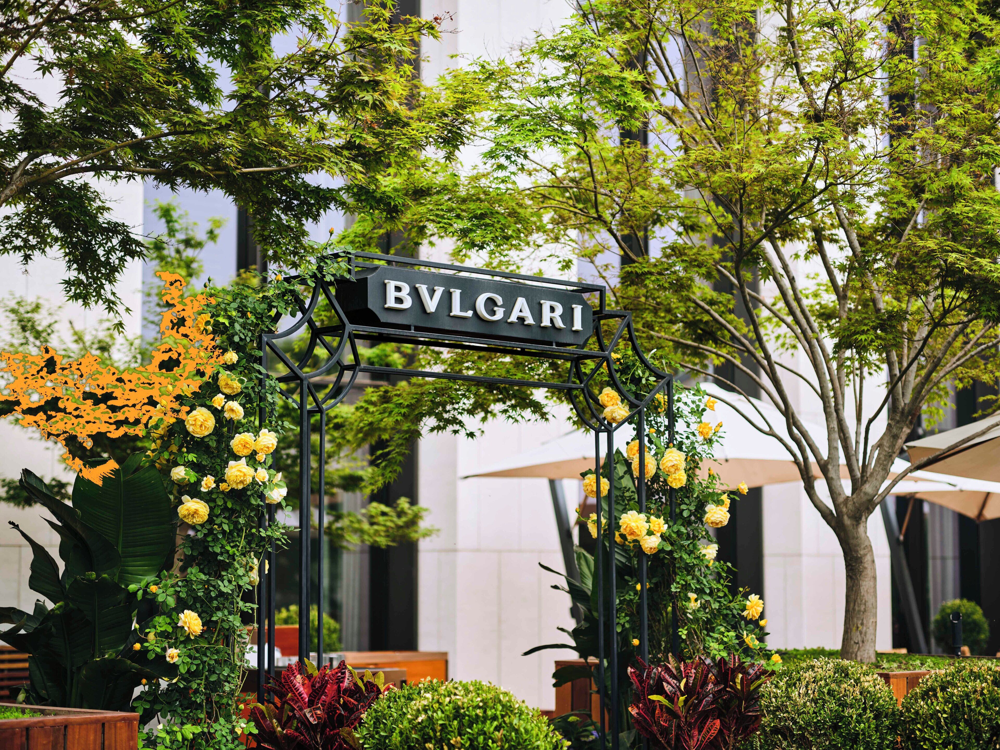 Ein Schild mit der Aufschrift "BVLGARI", umgeben von Grünpflanzen und Blumen.