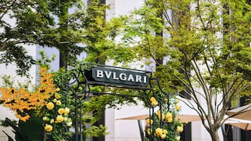 Een bord met de tekst 'BVLGARI', omgeven door groen en bloemen.