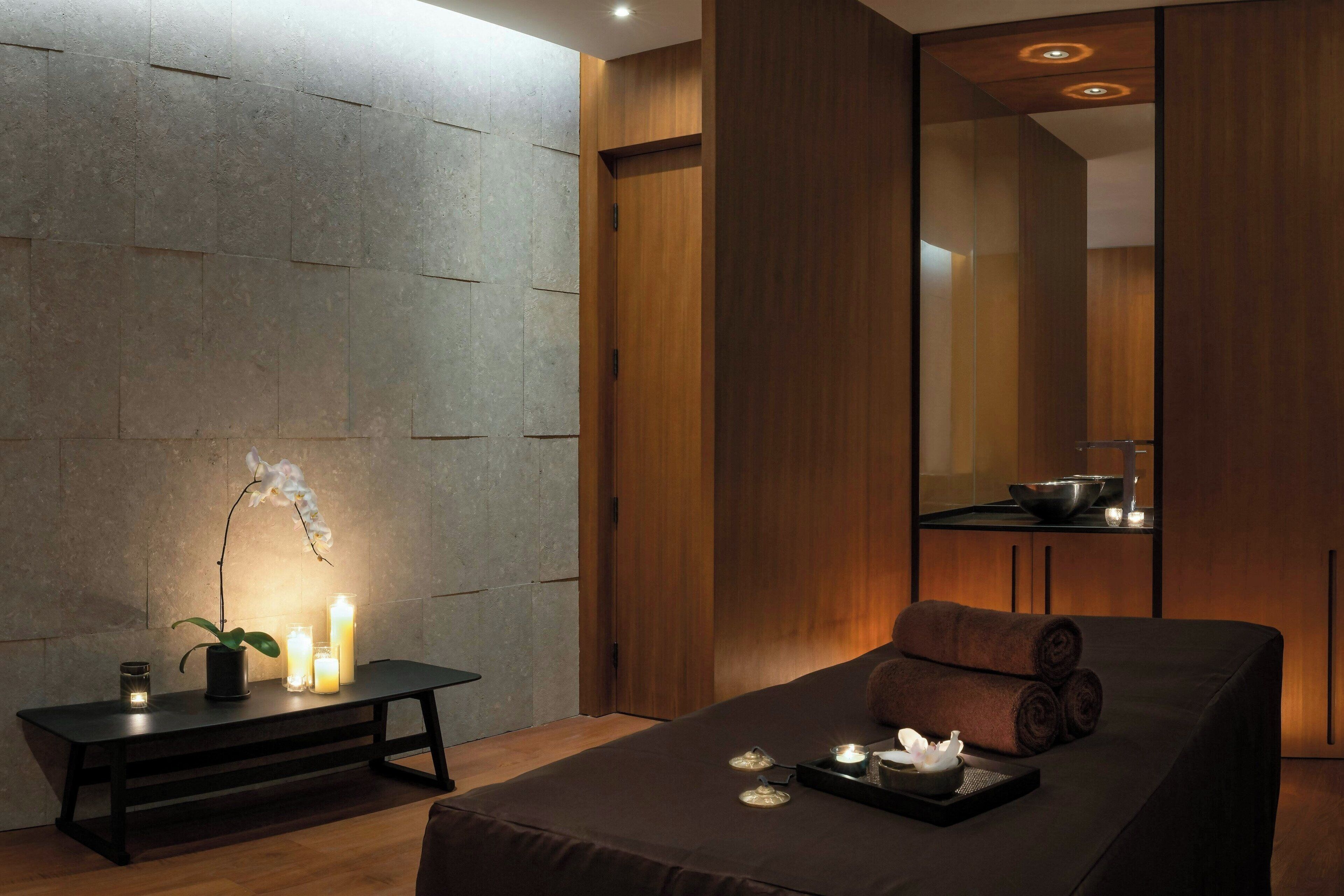 Ett spa-rum med en massagebänk, ljus och en orkidé i en kruka.