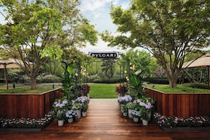 A wooden pathway leading to a sign that reads "BVLGARI" amidst lush greenery and potted plants. - Bvlgari Hotel Beijing (Beijing)