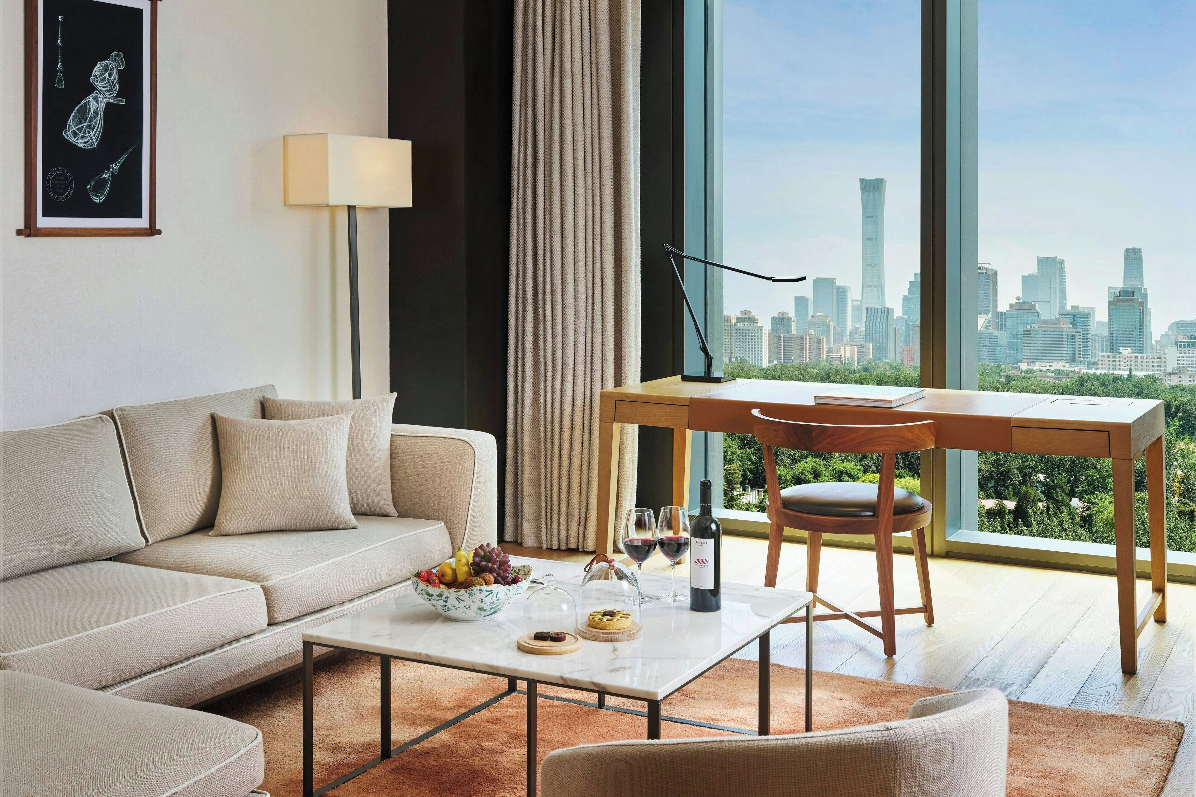 A modern living room with a sofa, coffee table, and dining table with chairs. A cityscape is visible through large windows.