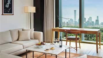 Una sala de estar moderna con sofá, mesa de centro y mesa de comedor con sillas. Se ve un paisaje urbano a través de amplias ventanas.