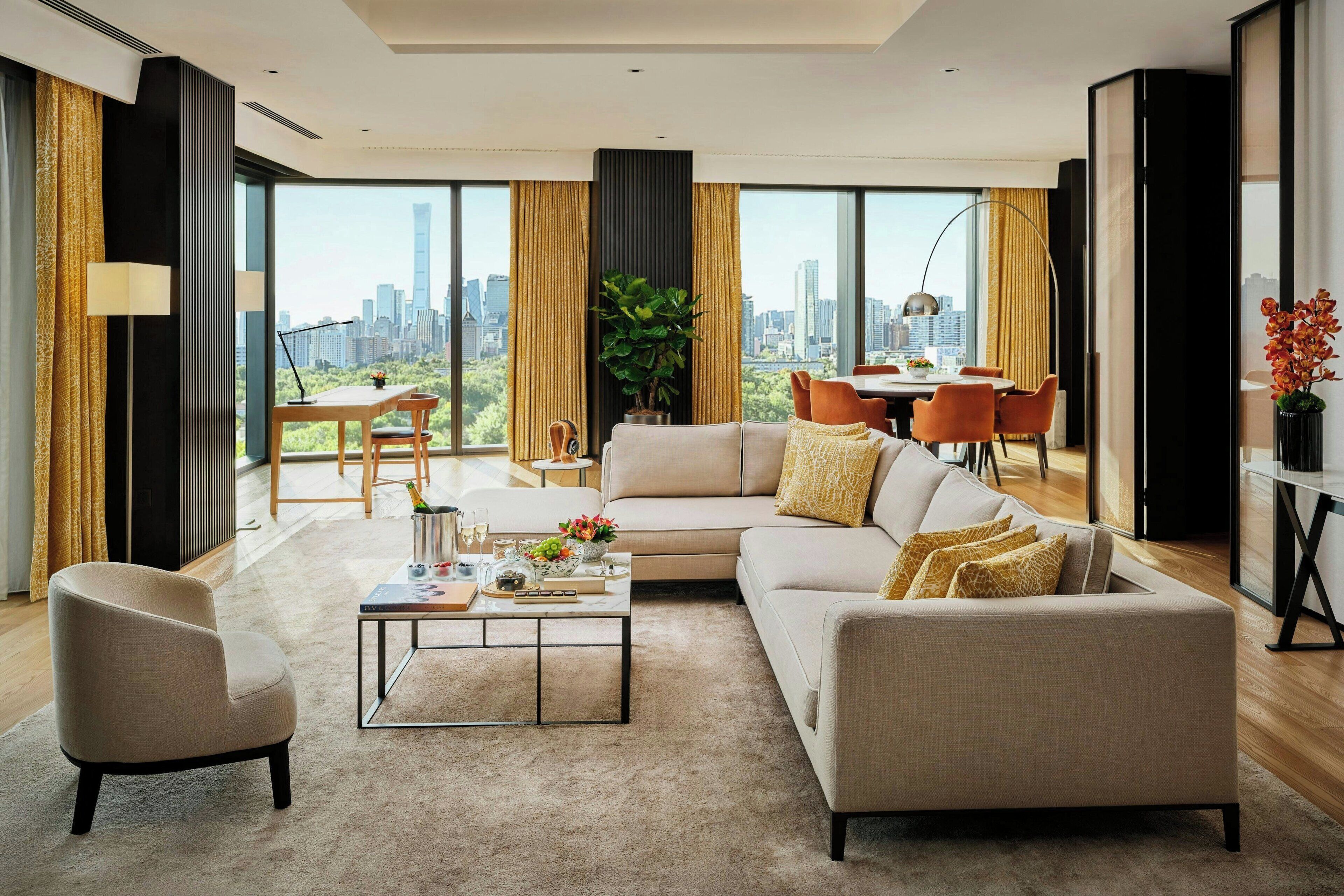 A modern living room with a sofa, armchair, and coffee table. A dining area with a table and chairs is visible in the background.