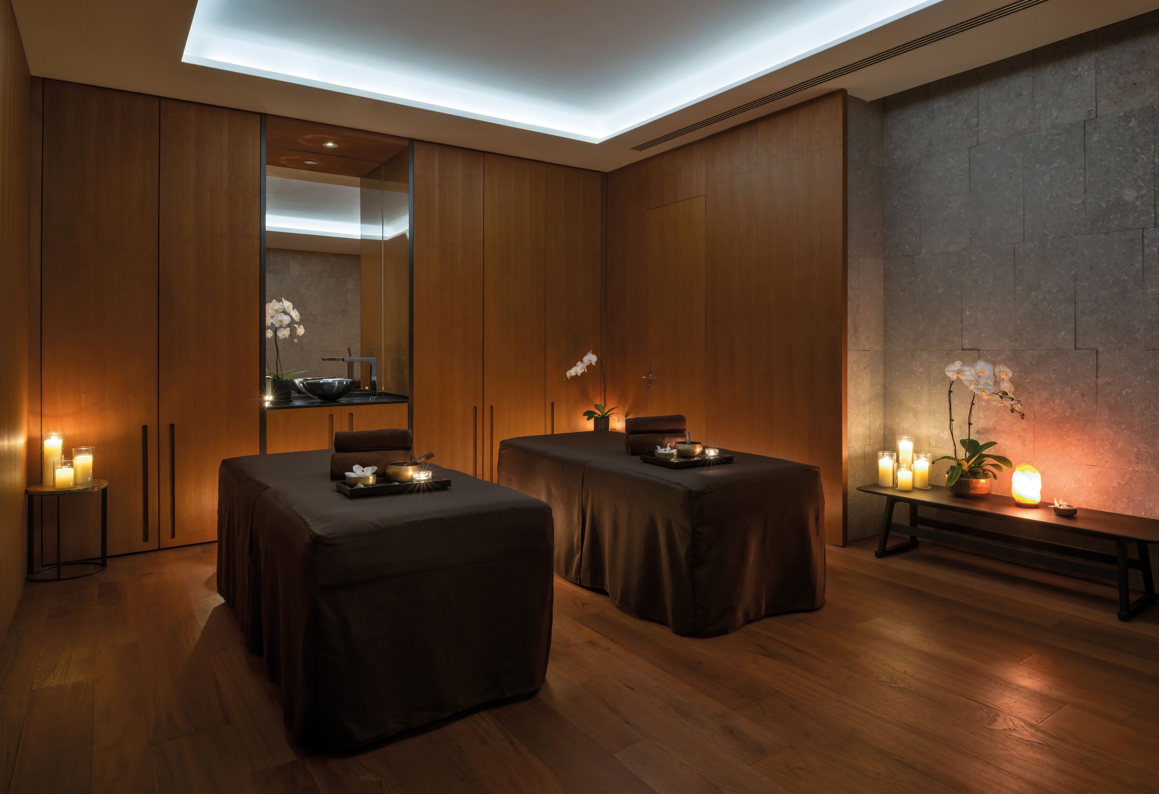 Ein Wellnessraum mit zwei Massagetischen, Holzboden und einem wandmontierten Spiegel.