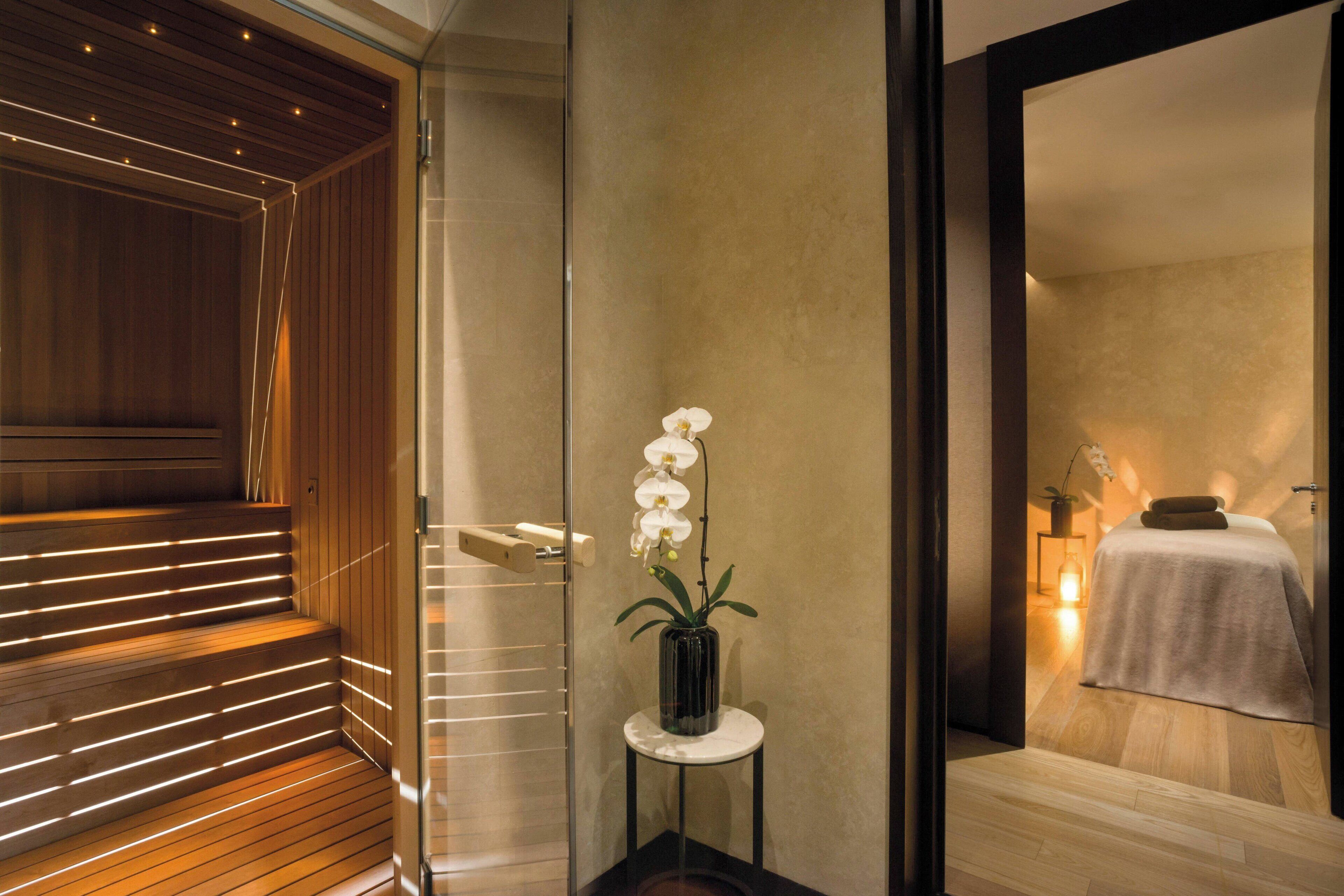 Una camera d'albergo moderna con una scala in legno, un divisorio in vetro e un piccolo tavolo con un'orchidea in vaso.