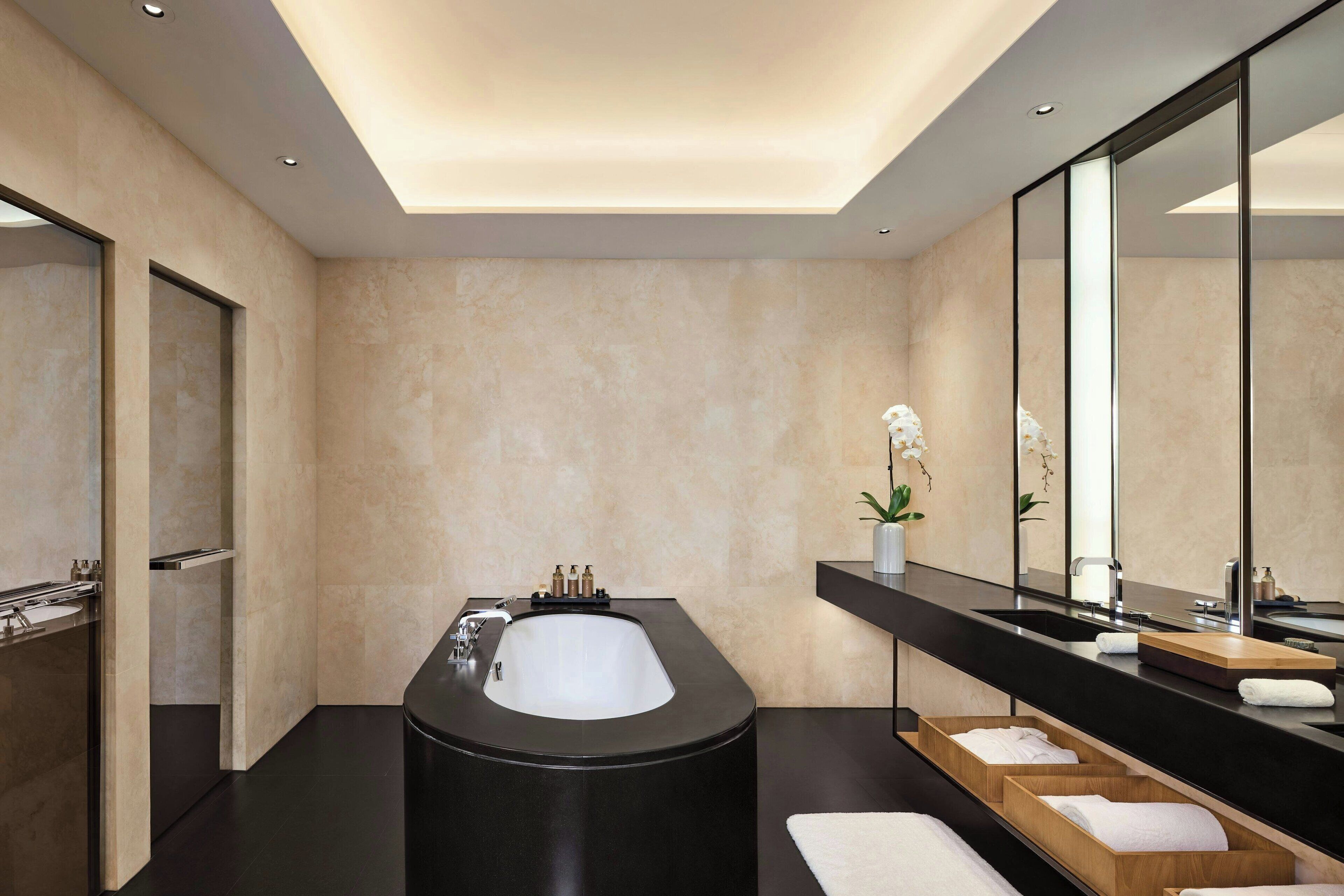 A modern bathroom with a large black bathtub, a mirror, and a wooden vanity with a sink.