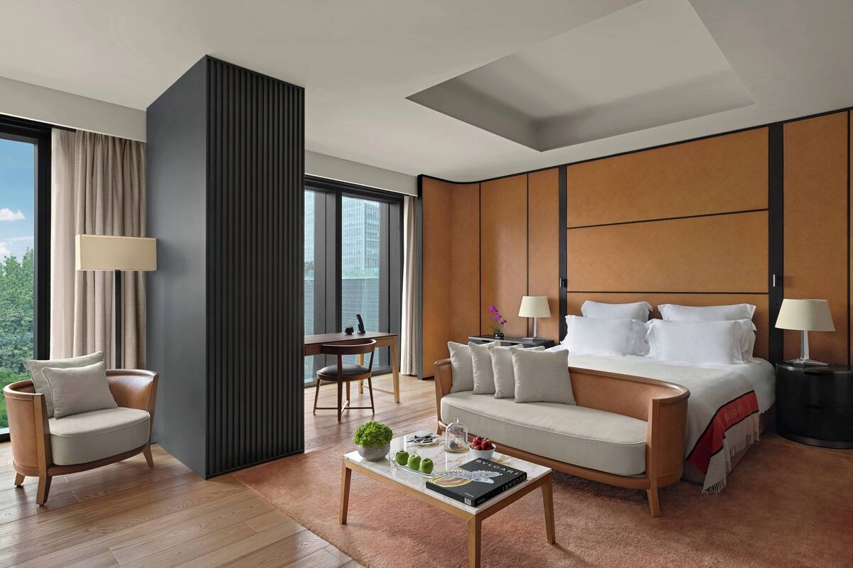 A modern hotel room with a large bed, a sofa, a coffee table with decorative items, a chair, and a desk.