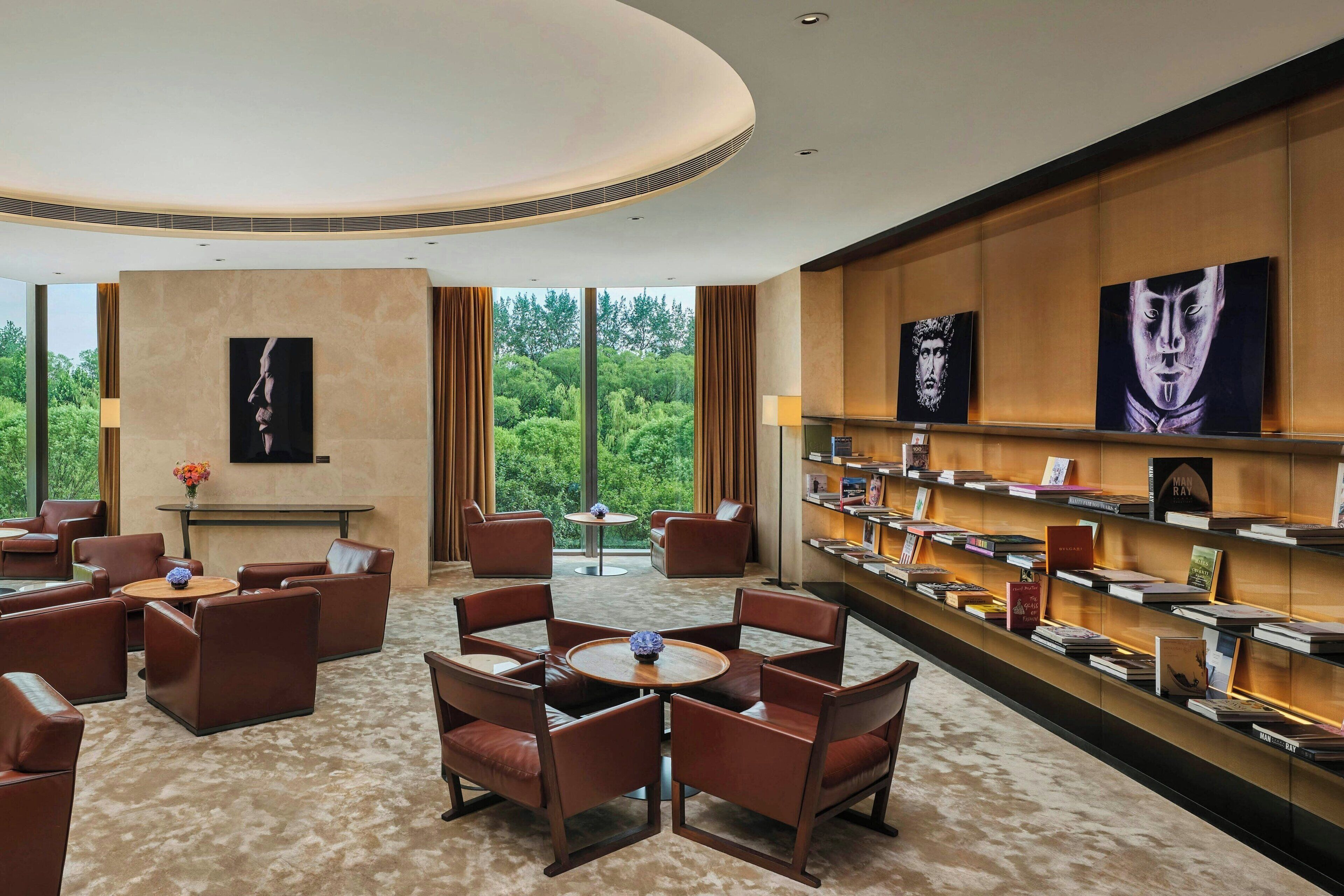 Een moderne hotellobby met lederen zitplaatsen, een centrale salontafel en een boekenkast met boeken.