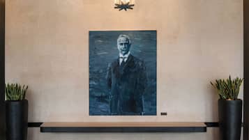 A portrait painting on a wall, flanked by two potted plants.