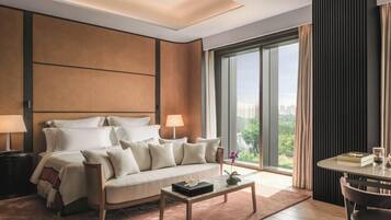 A modern hotel room with a large bed, a coffee table, a desk with a chair, and a large window offering a city view.