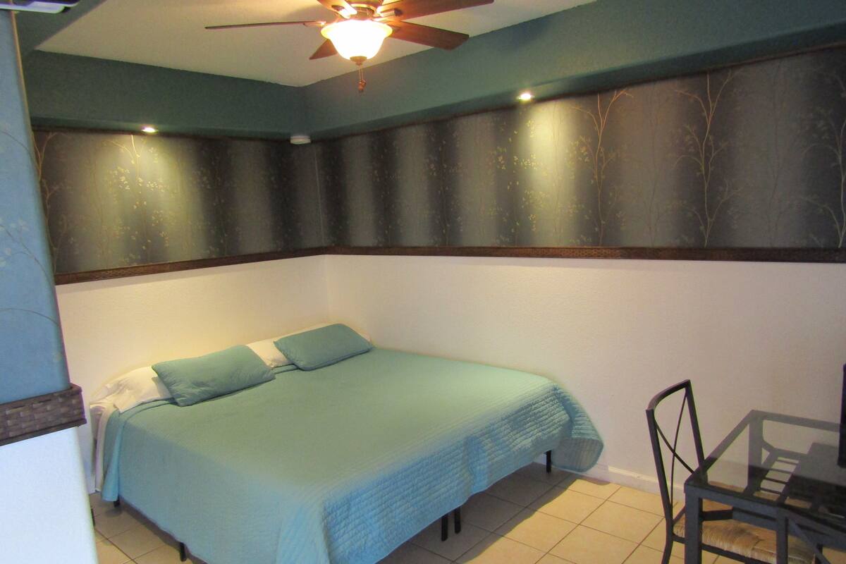 A bedroom with a bed, a chair, a ceiling fan, and a wall with a tree mural.