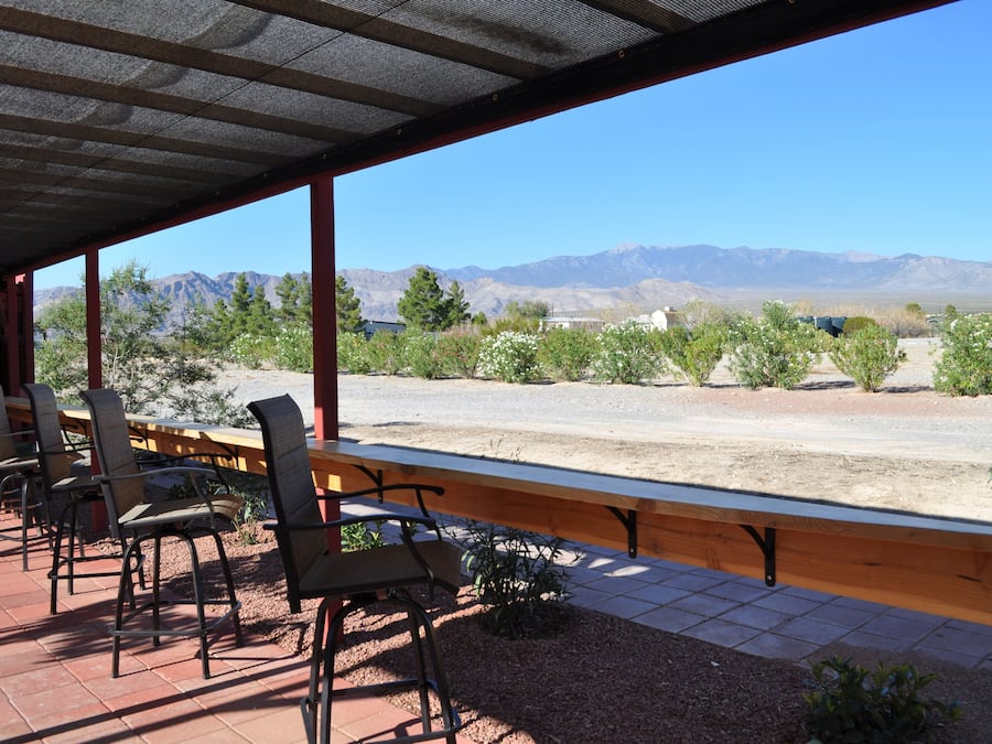An outdoor patio with a view of mountains, a covered seating area with chairs, and a wooden bench.