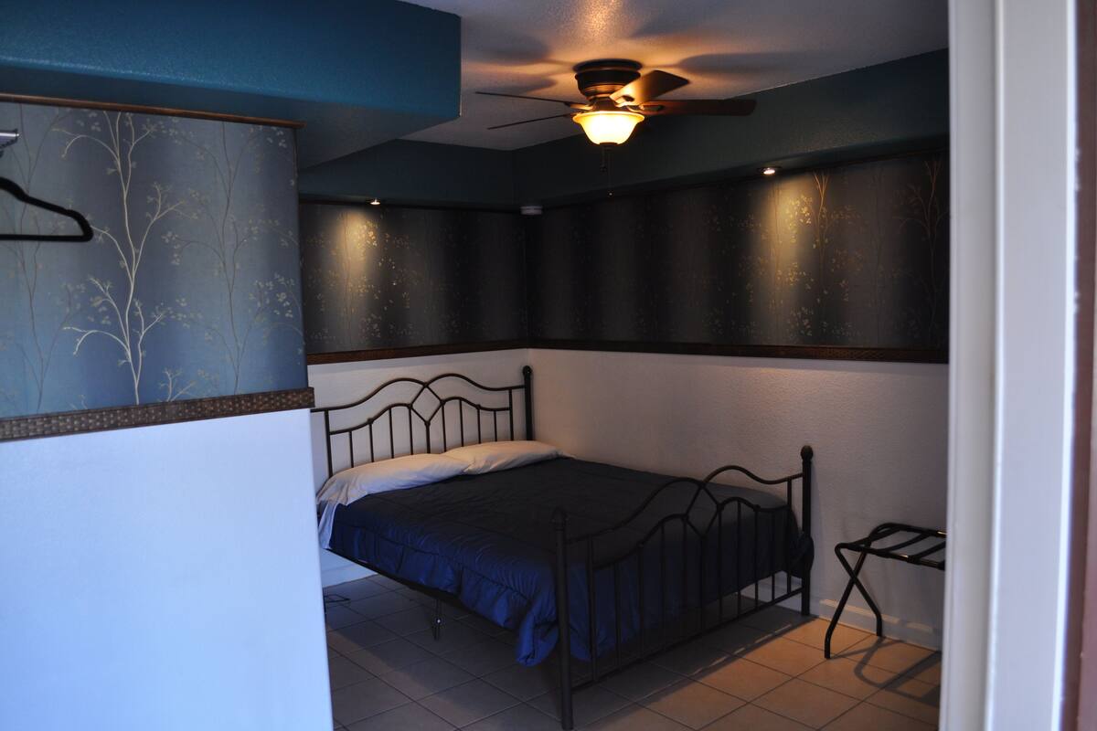 A bedroom with a single bed, a ceiling fan, and a wall-mounted shelf.