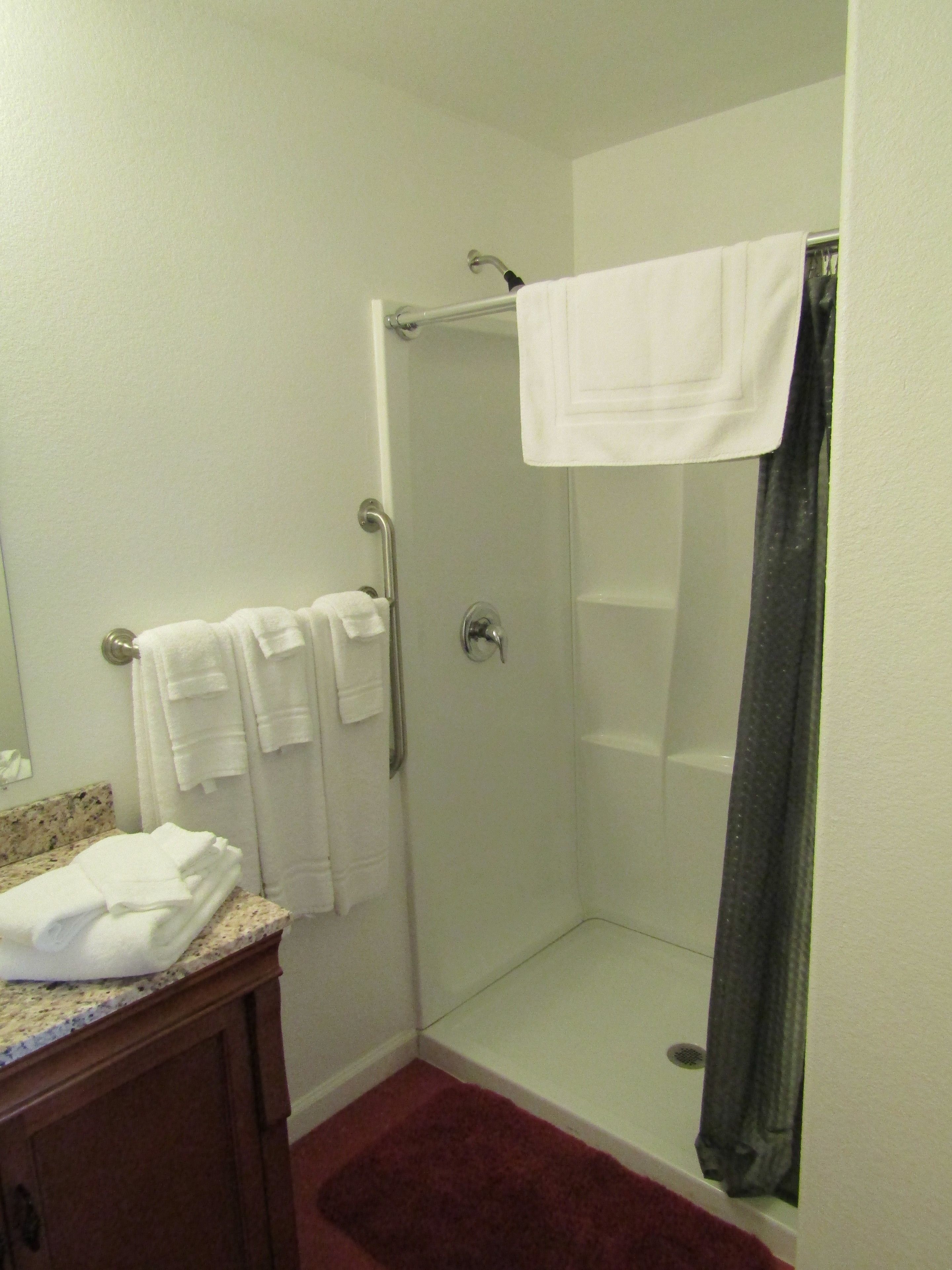 A bathroom with a shower, a sink with a marble countertop, and a wooden cabinet.