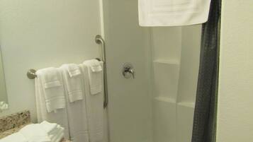 A bathroom with a shower, a sink with a marble countertop, and a wooden cabinet.