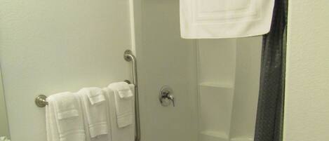 A bathroom with a shower, a sink with a marble countertop, and a wooden cabinet.
