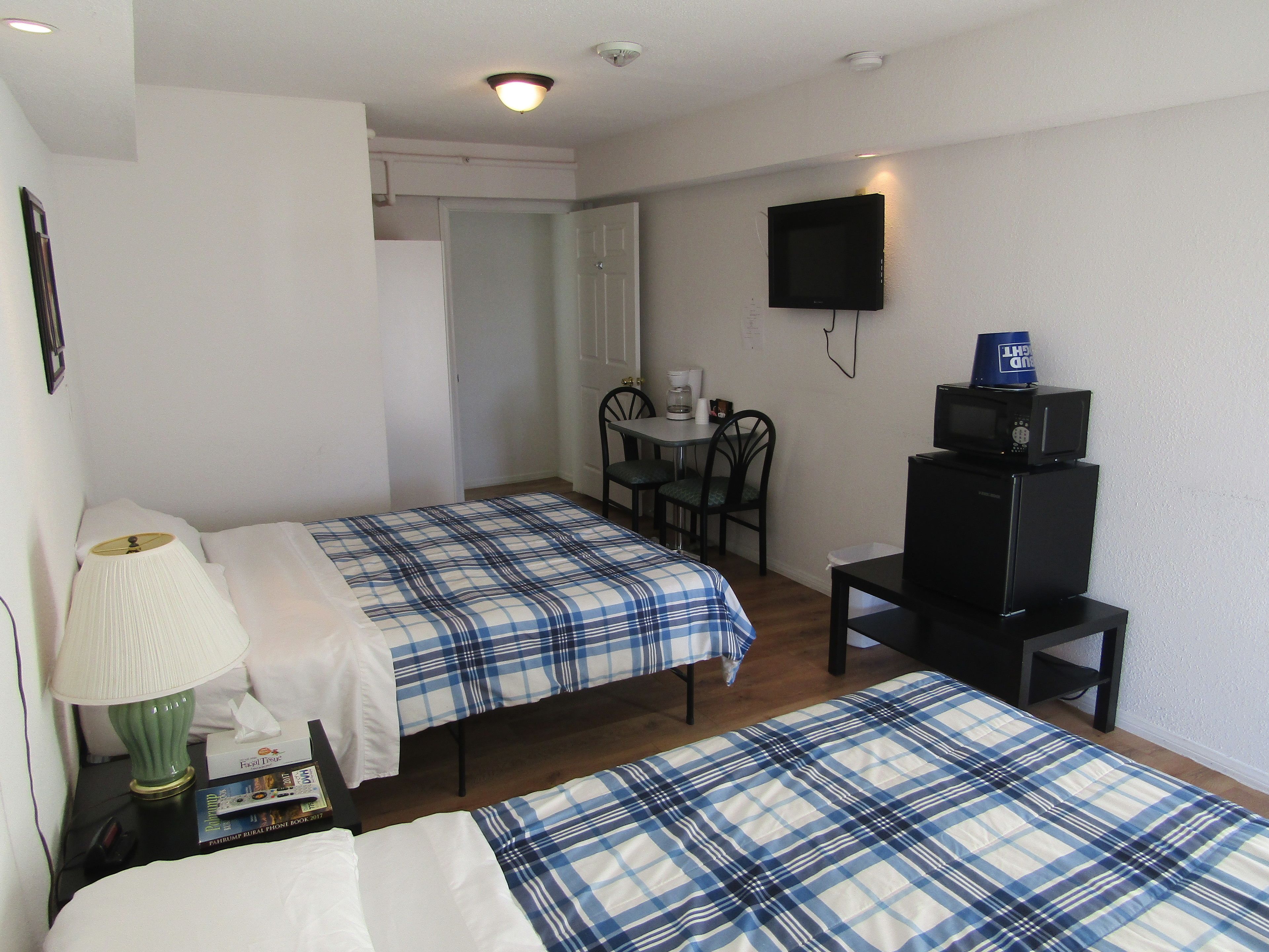 A room with two beds, a desk, a chair, a television, and a lamp.