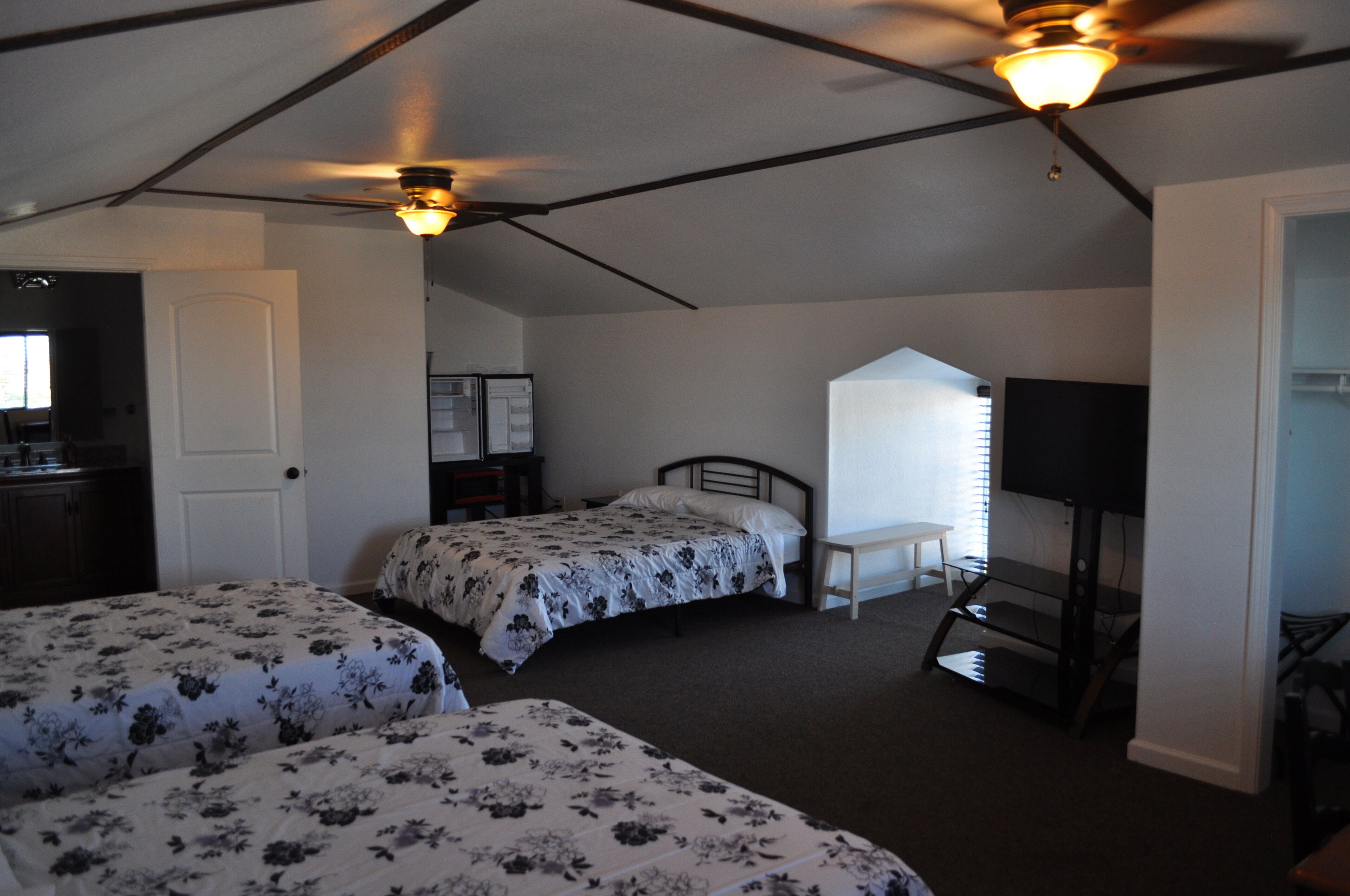 A bedroom with two beds, a ceiling fan, a television, and a desk.