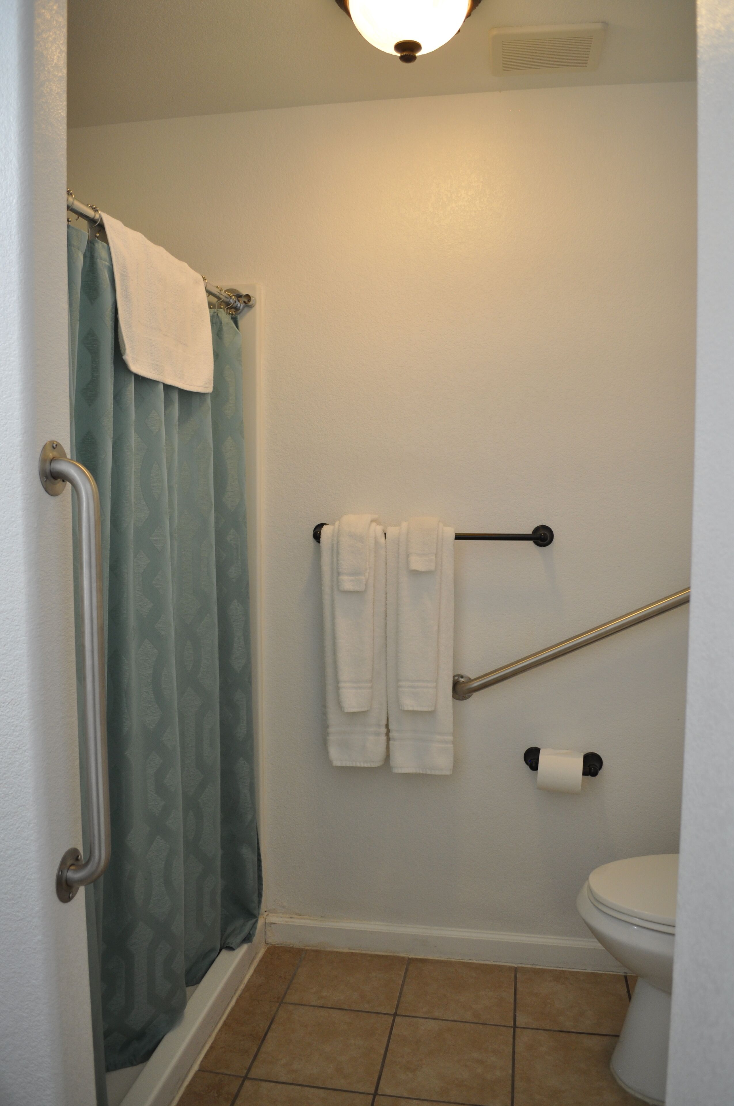 A bathroom with a shower curtain, a toilet, a grab bar, and two towels on a rack.