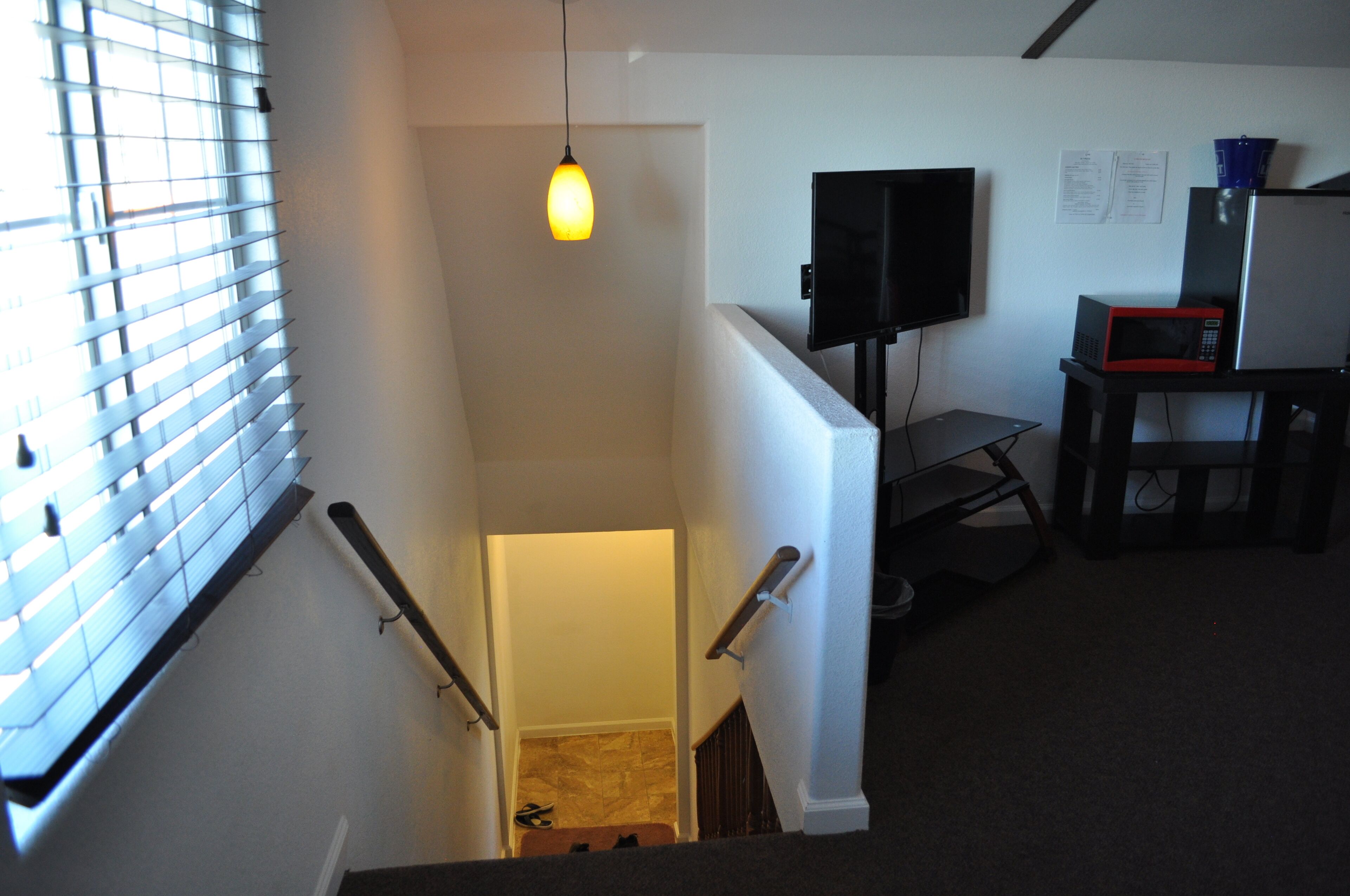A staircase with a hanging light fixture, a flat-screen TV mounted on the wall, and a microwave on a small table.