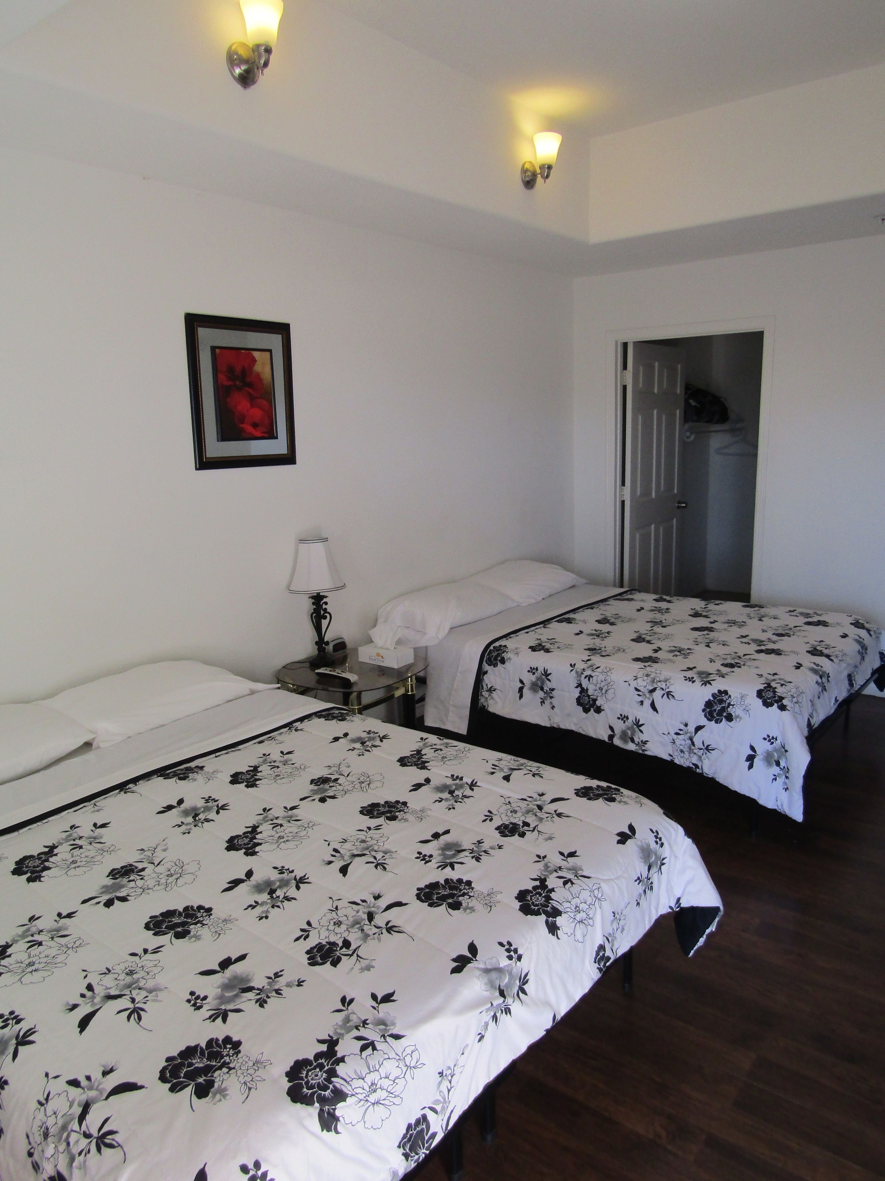 A hotel room with two beds, a nightstand, a framed picture on the wall, and a door leading to a bathroom.