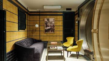 A room with a black sofa, yellow chairs, a glass coffee table, and a framed picture on the wall.