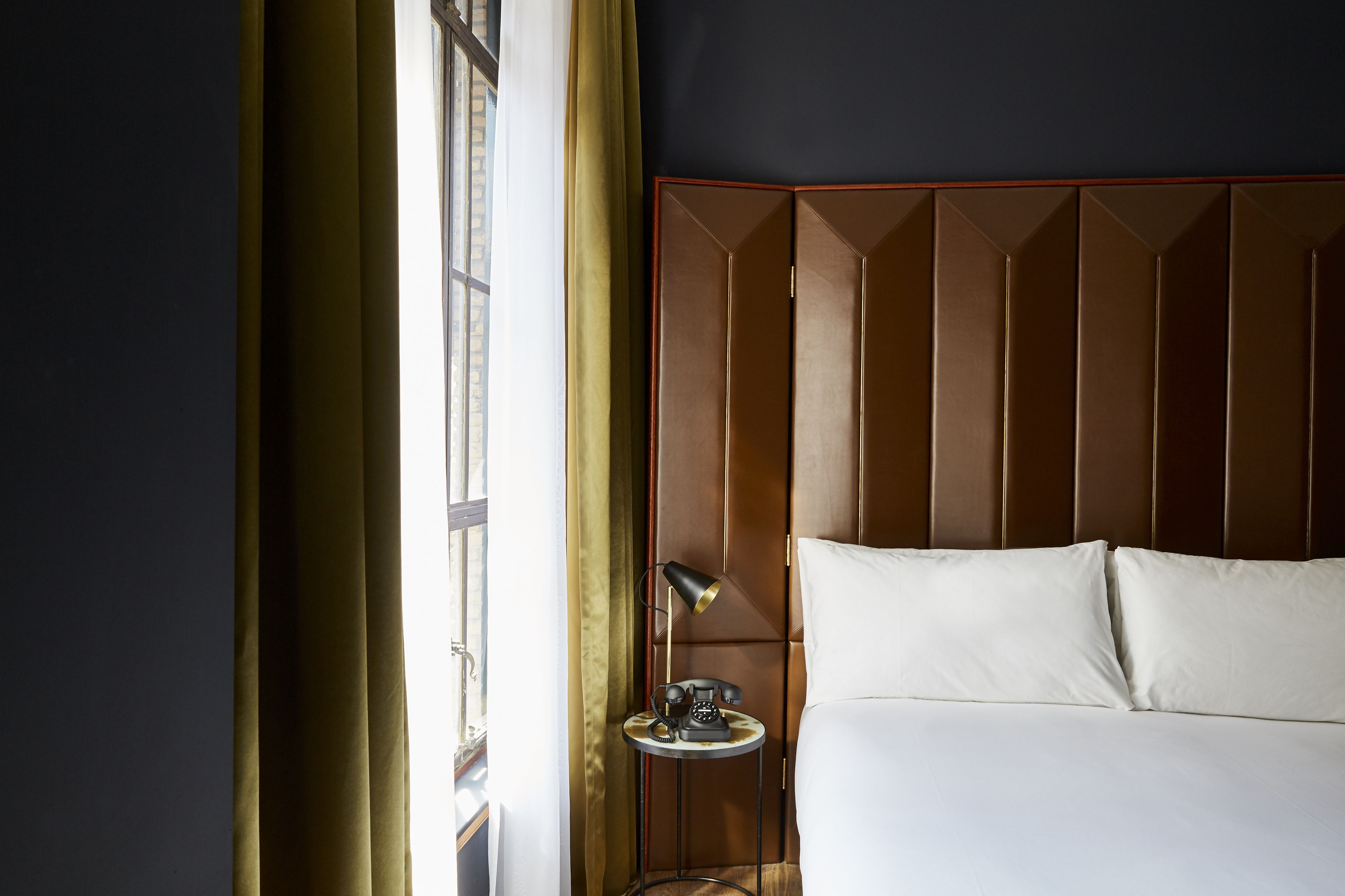 A hotel room with a bed, a bedside table with a lamp, and a window with curtains.