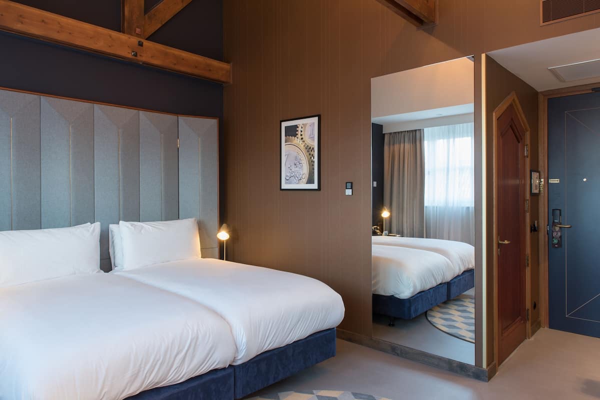 A hotel room with a large bed, a mirror, a wooden ceiling, and a door.