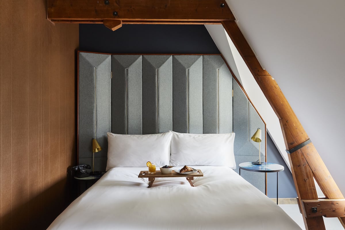 A neatly made bed with a tray of breakfast items, a bedside lamp, and a small table with a lamp.