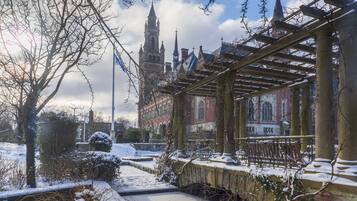 Un'area esterna innevata con un pergolato in legno, un edificio in mattoni con una torre e un cielo sereno.