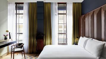 A hotel room with a bed, a desk, a chair, and a large window with curtains.