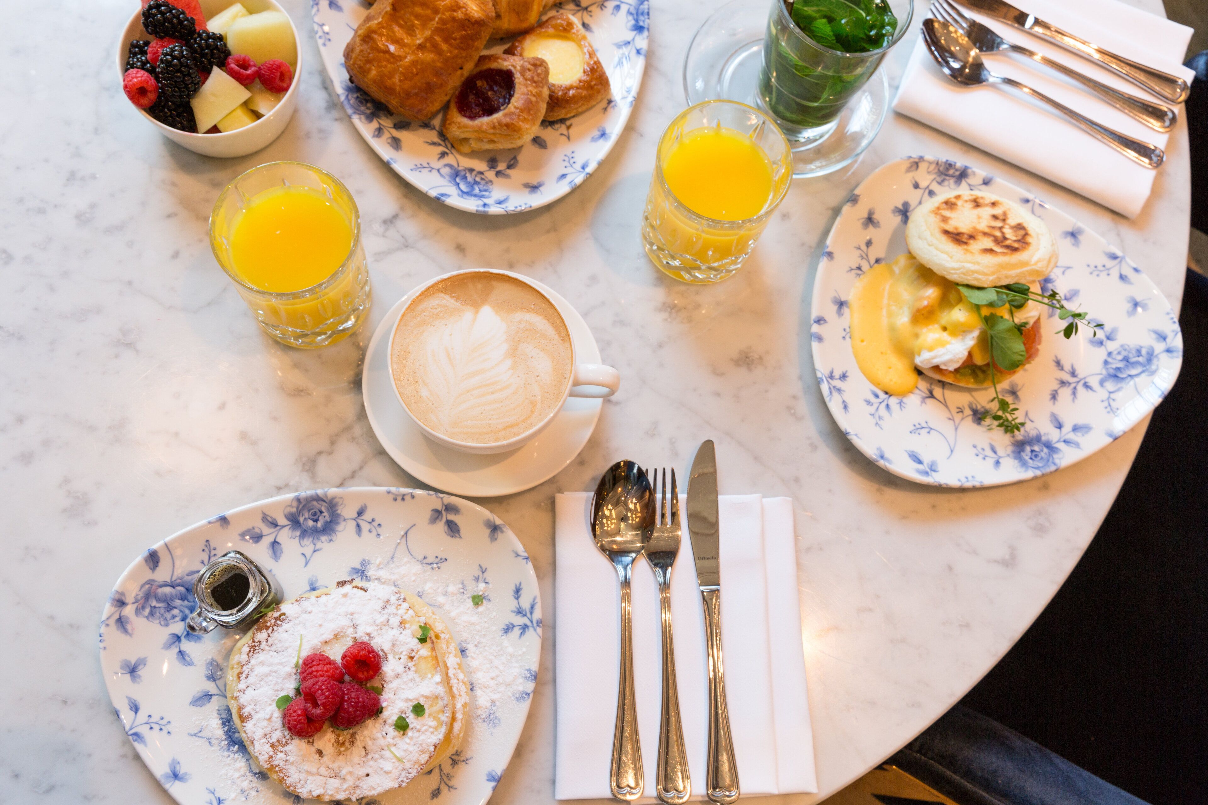 A breakfast setting with various dishes, including pastries, fruits, and beverages on a marble table.
