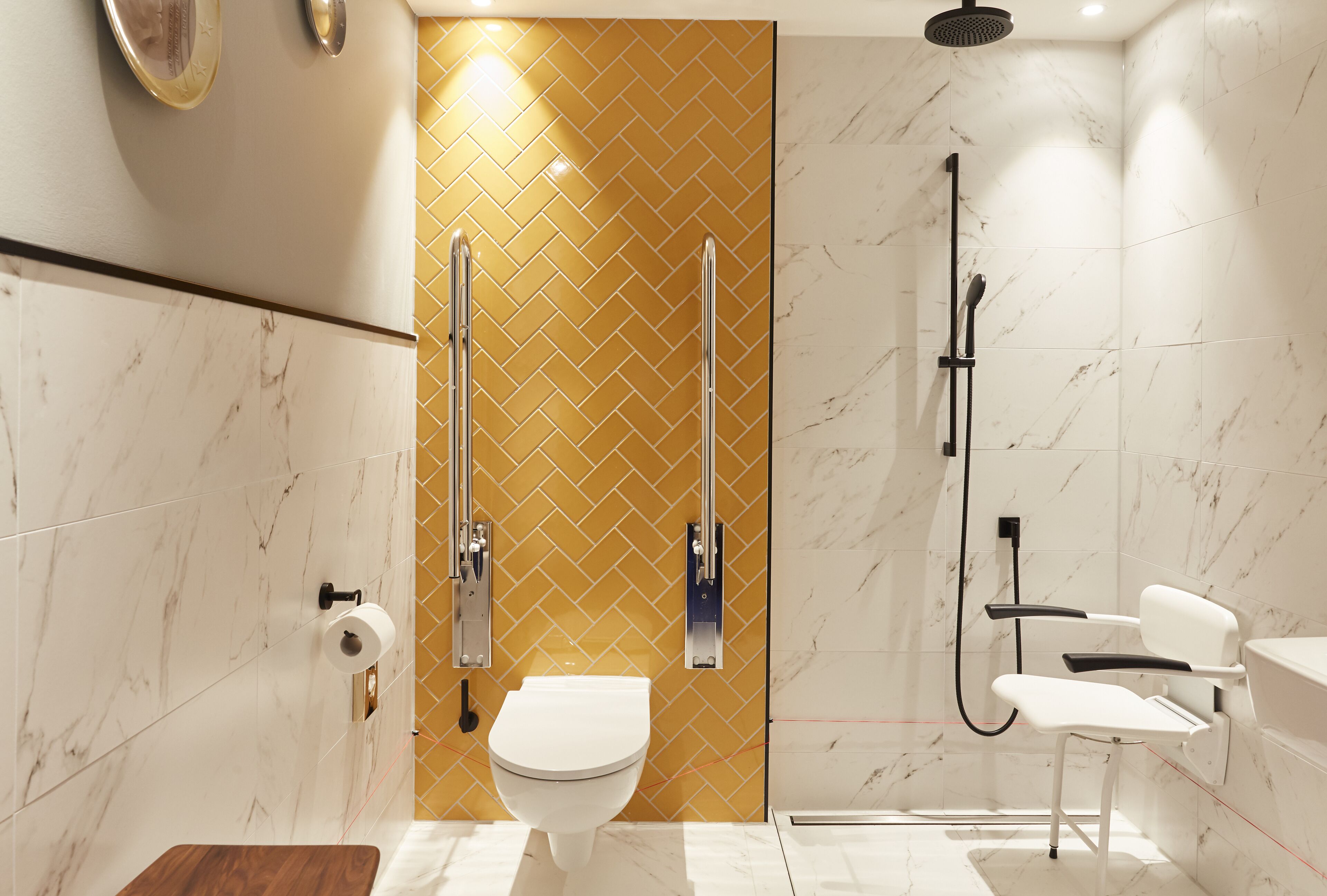 Un baño moderno con inodoro blanco, ducha con cabezal de ducha manual y tocador con espejo.