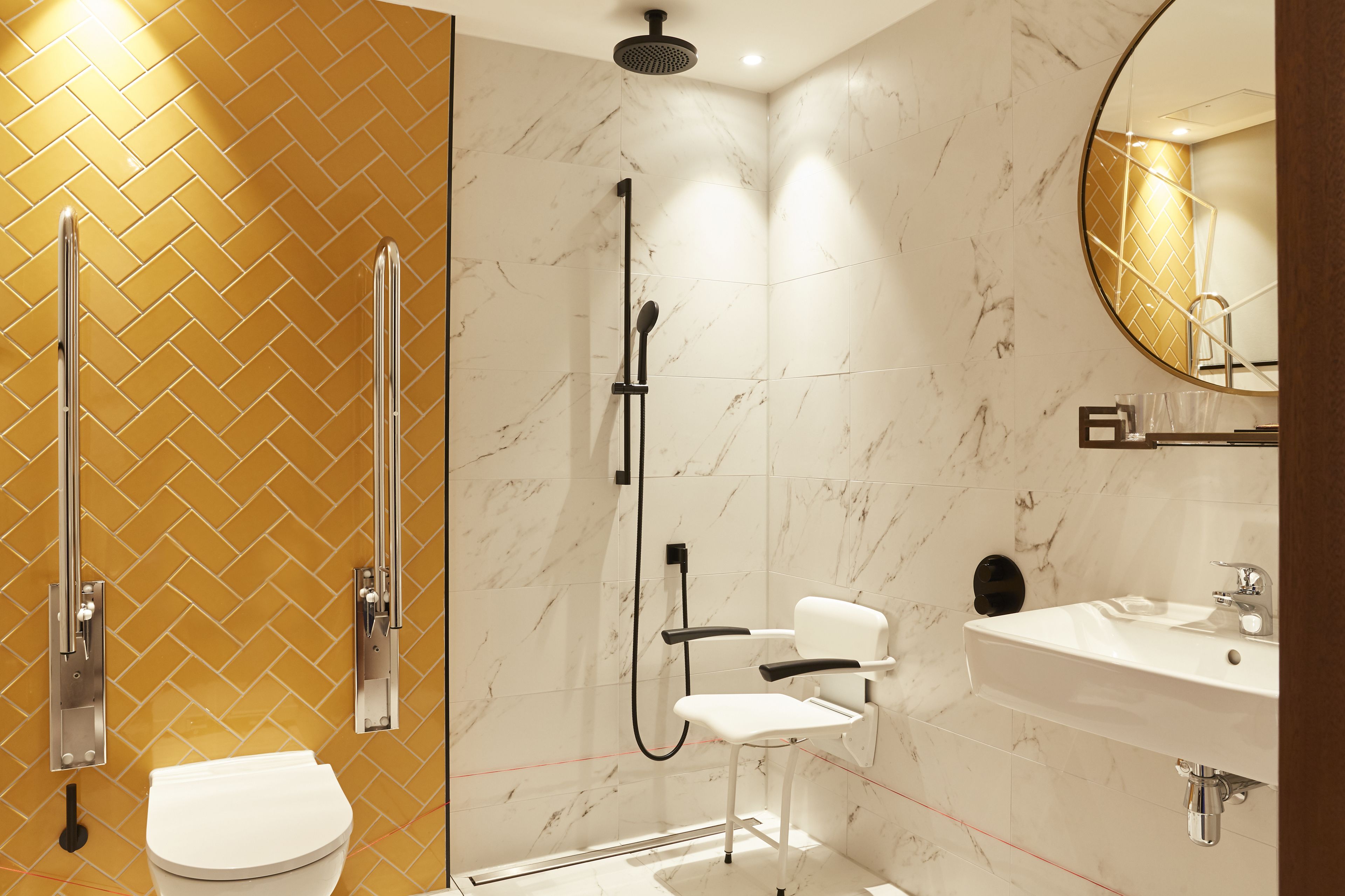 A modern bathroom with a herringbone tile pattern, a white toilet, a shower with a handheld showerhead, and a sink with a mirror above it.