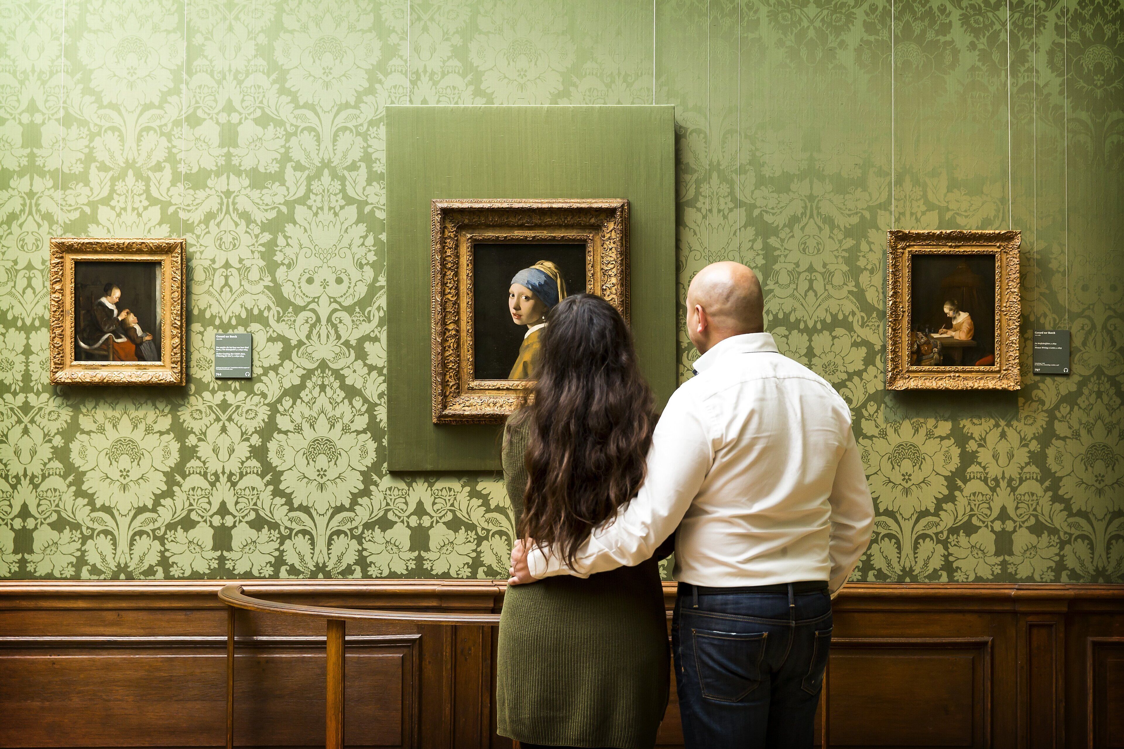 Un couple se tient devant des tableaux encadrés accrochés à un mur vert à motifs.