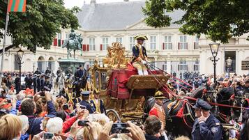 Un desfile histórico con un carruaje dorado y participantes uniformados.