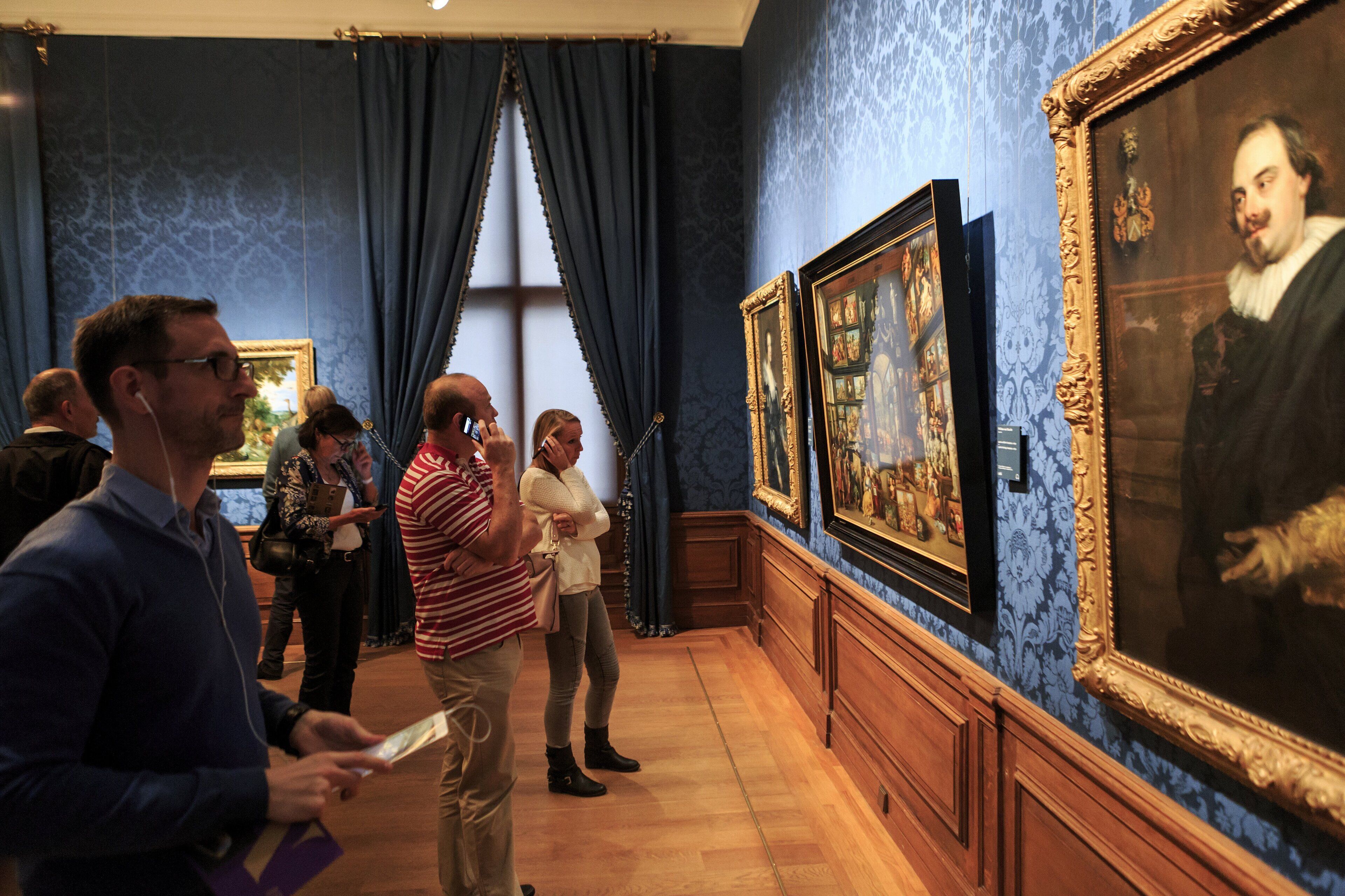 A gallery with framed paintings on the walls, wooden paneling, and a blue patterned wall.