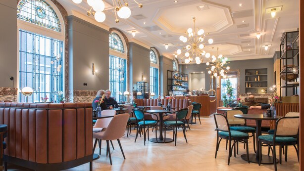 Ein geräumiges Restaurant mit hohen Decken, großen Fenstern und einem zentralen Kronleuchter.