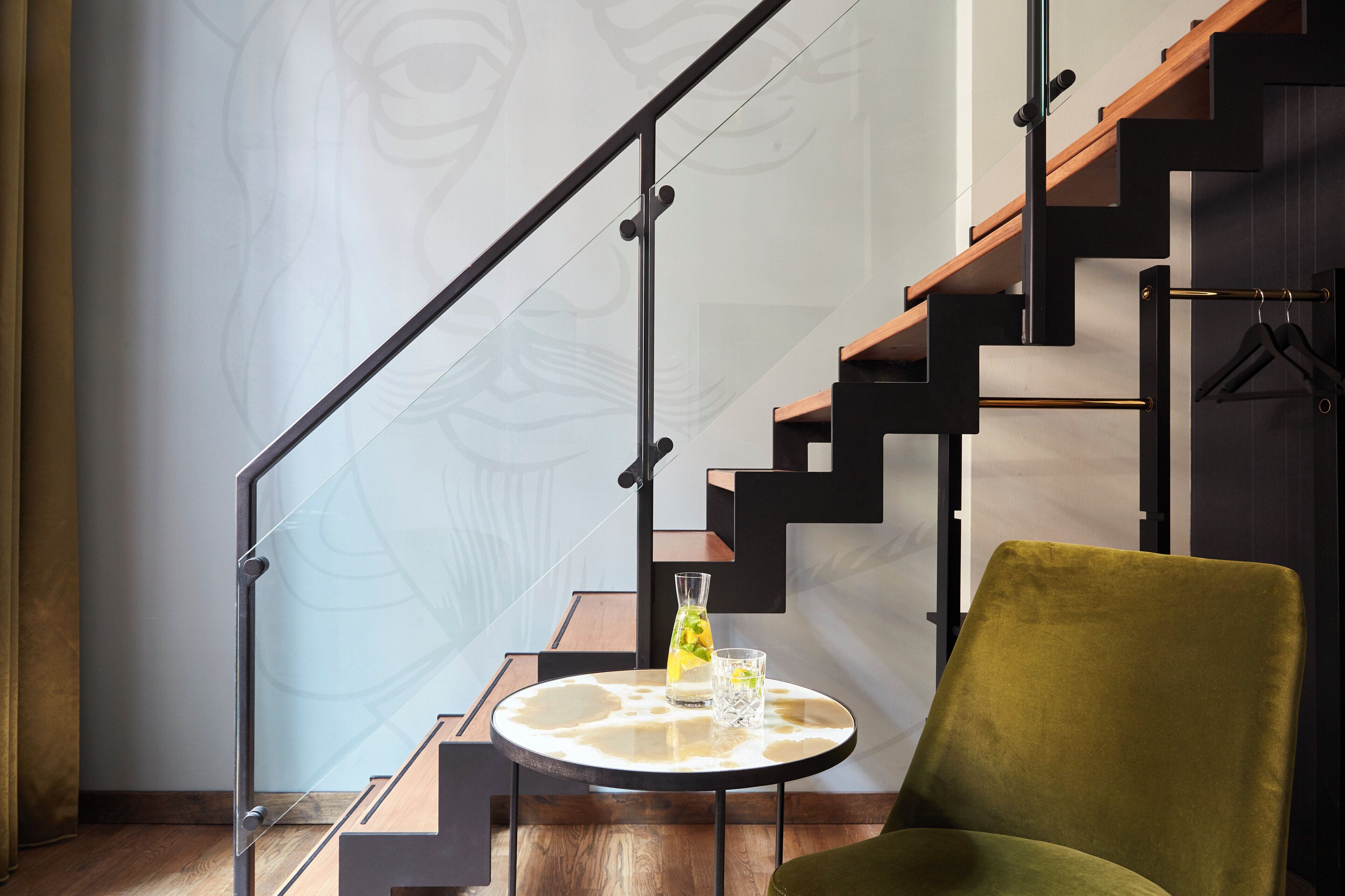 Un interior moderno con una escalera, una mesa redonda con vasos y una silla verde.