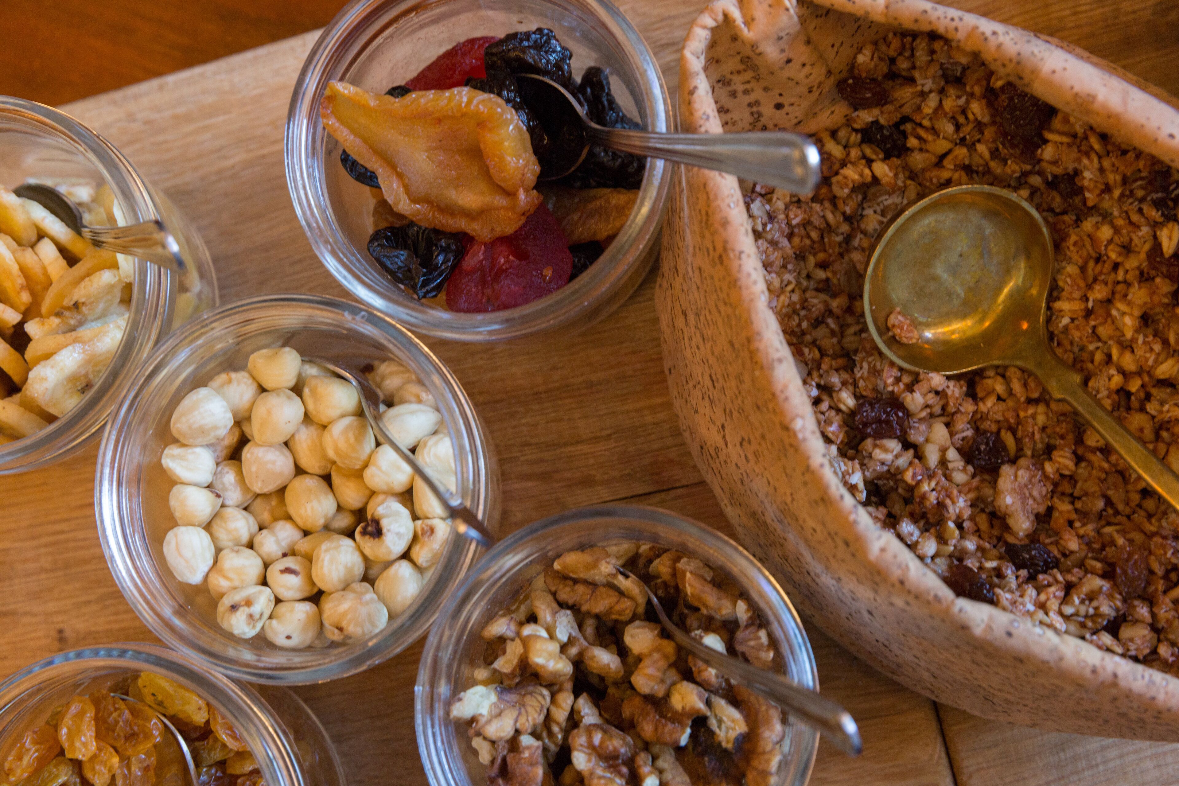 A wooden table with various bowls containing nuts, dried fruits, and granola.