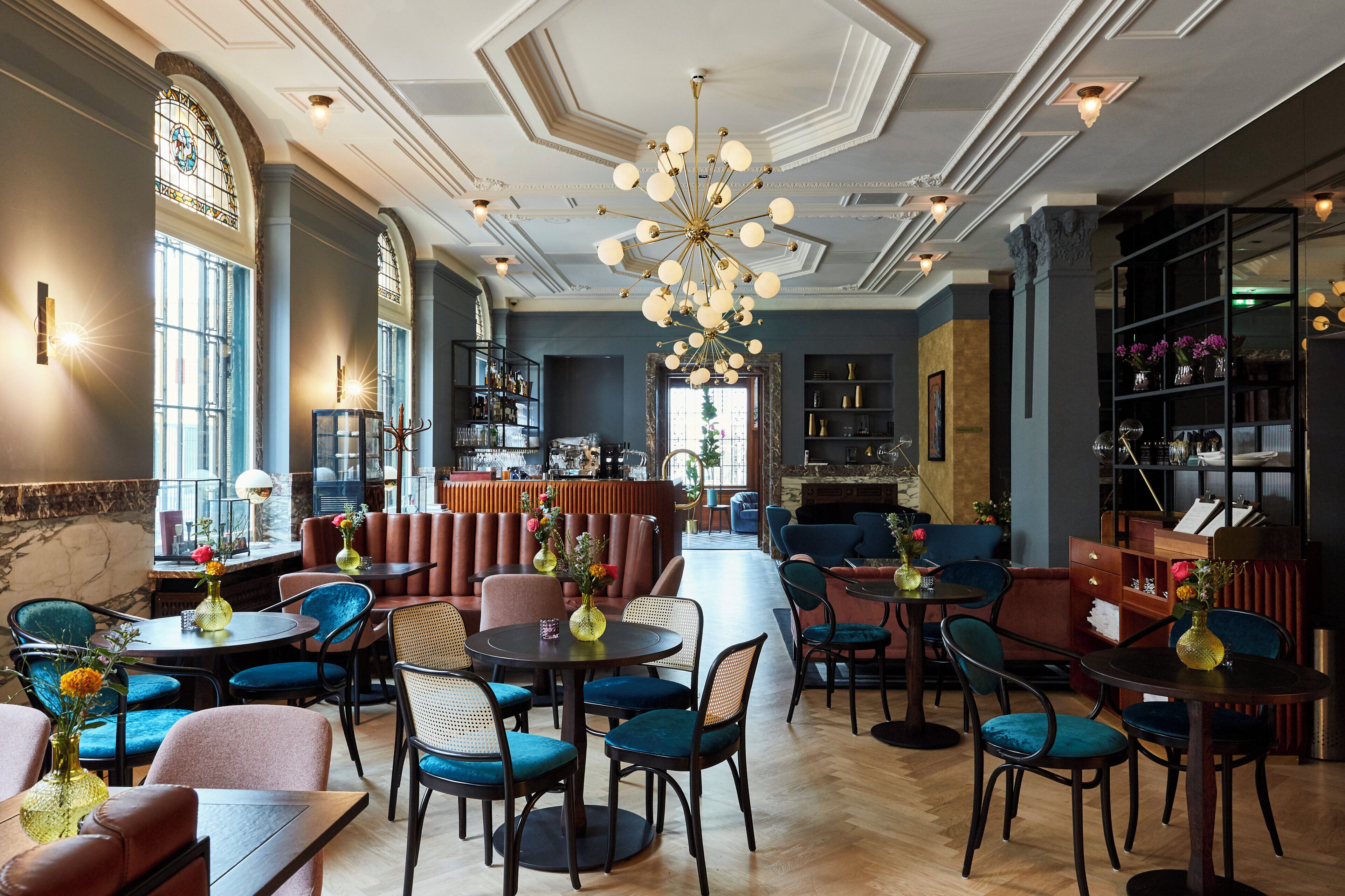 Un comedor amplio con varias mesas y sillas, un candelabro y una zona de bar con estantes llenos de botellas.