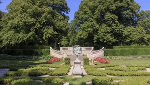 Un jardin à la française avec une fontaine centrale, des pelouses parfaitement entretenues et de grands arbres.