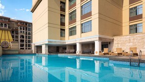 A hotel pool area with clear blue water, sun loungers, and a large building with multiple floors and windows. - Wyndham Garden Foshan Nanhai (Foshan)