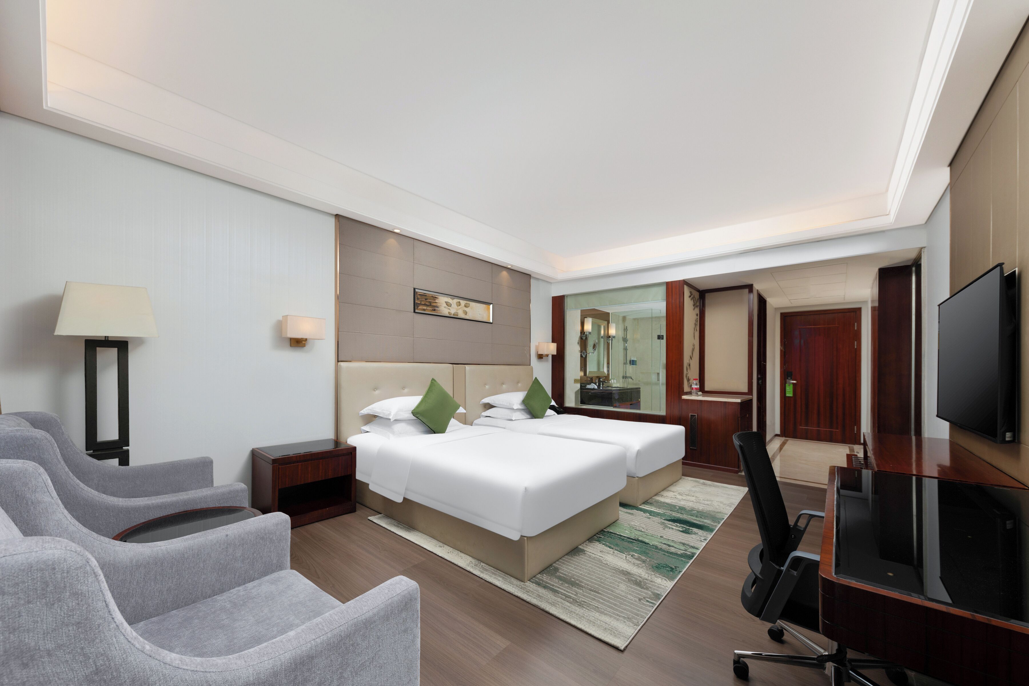 A hotel room with a large bed, two bedside tables, a desk with a chair, a TV, and a seating area with chairs.