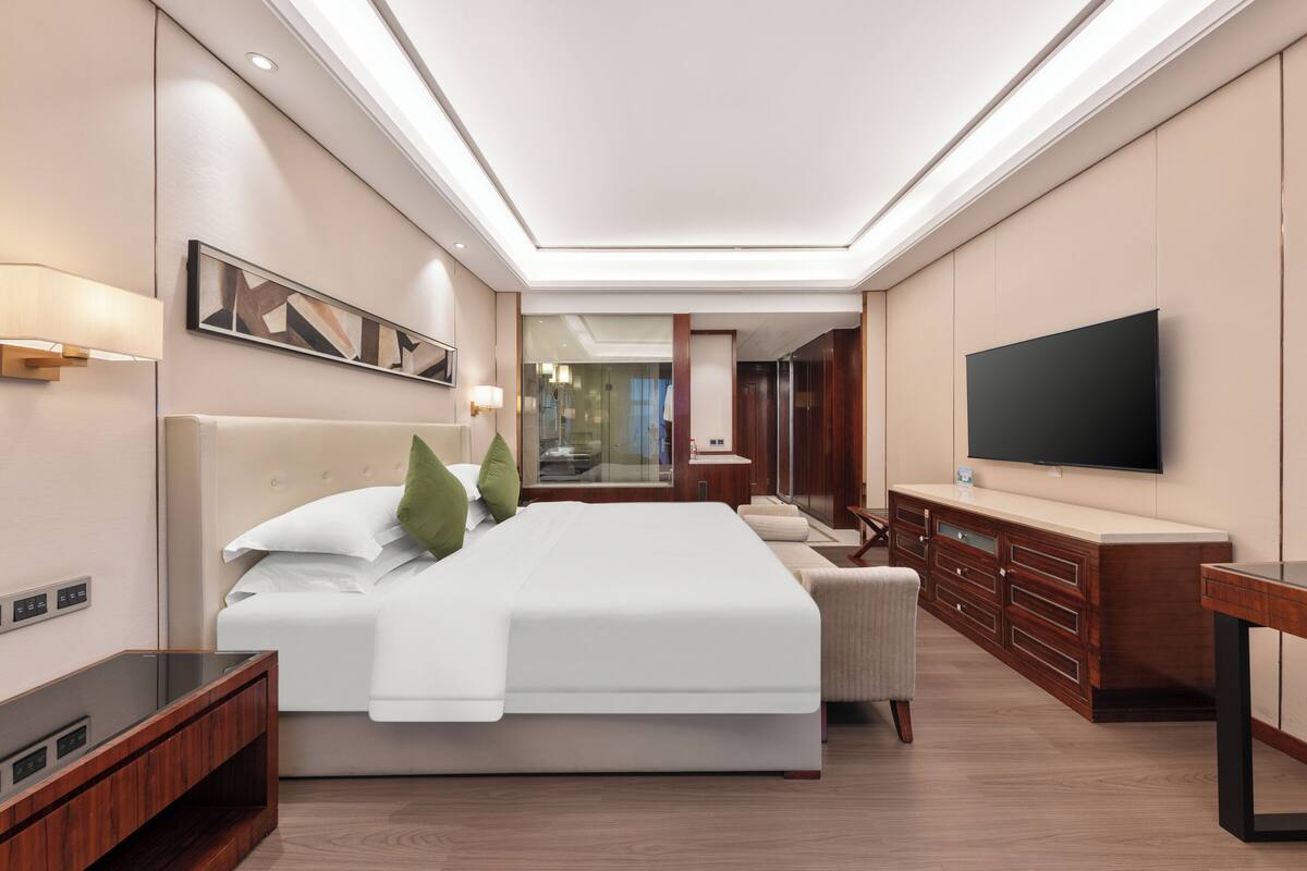 A modern hotel room with a large bed, a TV, a wooden dresser, and a mirror.