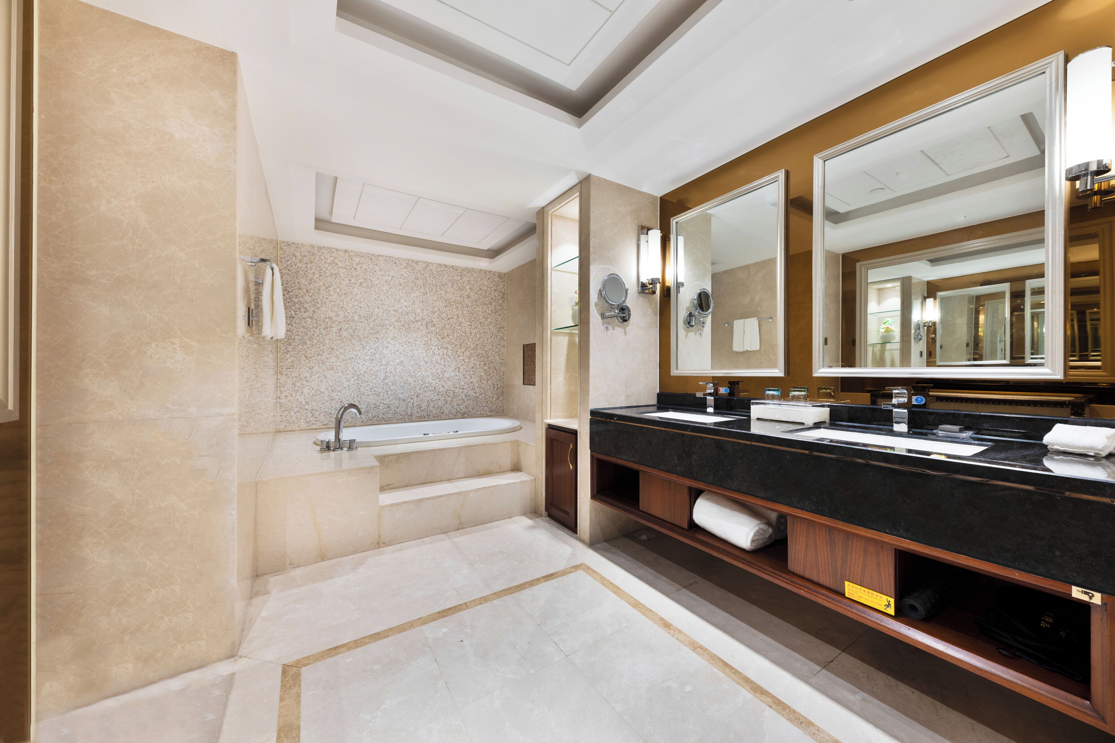 A modern bathroom with a bathtub, double sink, and large mirrors.