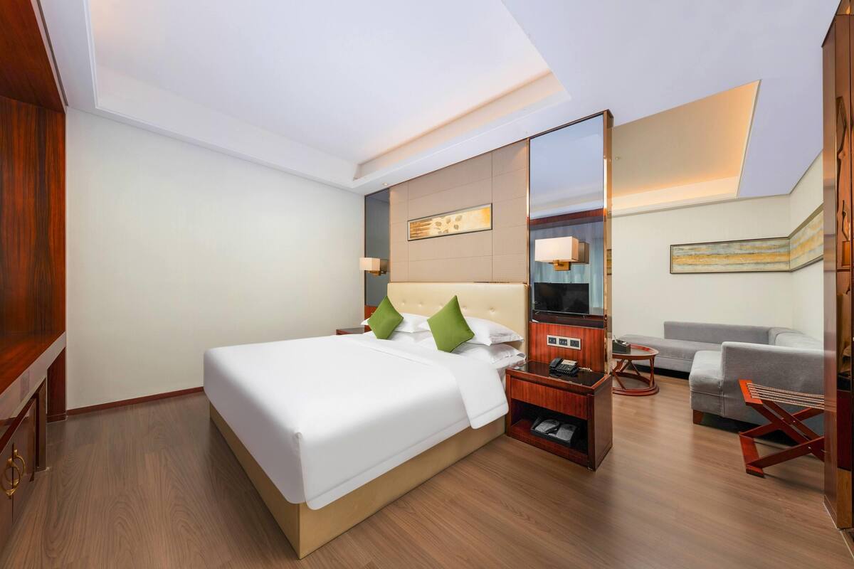 A hotel room with a large bed, a bedside table, a mirror, a sofa, and a small table.