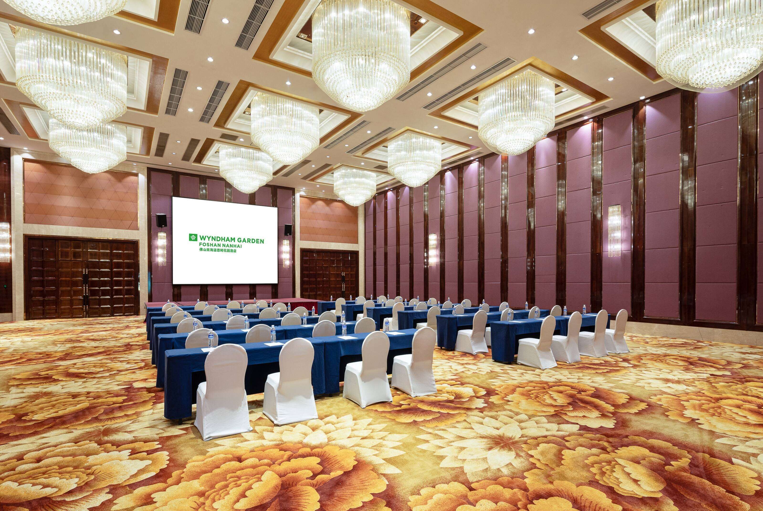 A conference room with rows of tables and chairs, a large screen, and chandeliers.