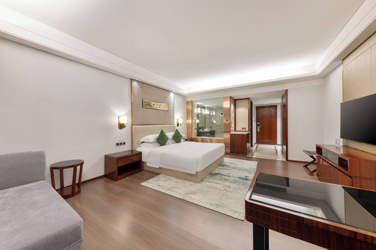 A modern hotel room with a bed, a TV, a desk, and a seating area.