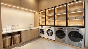 A laundry room with four washing machines, wooden cabinets, and storage shelves.